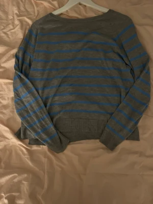 Gråblå randig tröja från Zara - Säljer en grå tröja från Zara i storlek M med blåa horisontella ränder. Tröjan har lång ärm, rund halsringning och ribbade muddar. Materialet är en mjuk blandning av viskos och akryl, perfekt för lager på lager under kyligare dagar.