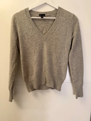 Beige v-ringad tröja från GANT - Snygg beige v-ringad tröja från GANT i mjuk ullmix. Tröjan har långa ärmar och ribbade muddar vid ärmslut och nederkant. Perfekt för lager-på-lager och passar till jeans eller kjol. Enkel och stilren design som funkar året runt.