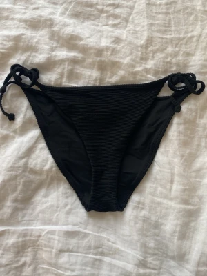 Svarta bikiniunderdelar med knyt - Säljer en svart bikiniunderdel med ribbad struktur och knytning i sidorna. 