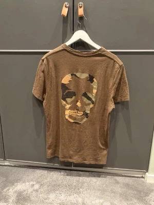 Brun t-shirt med camo dödskalle Zadig & Voltaire - Brun-grön t-shirt från Zadig & Voltaire med en riktigt fet design. Storleken är M. Mitt pris är 480 vilket jag anser som ett väldigt bra pris för en sällsynt t-shirt! Finns det något du undrar över är det bara att fråga!