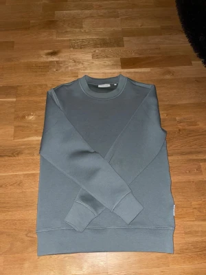 Balsam Grön sweatshirt från Casual Friday - En stilren grå sweatshirt från Casual Friday i storlek S. Tröjan har rund halsringning, ribbade muddar vid ärmslut och nederkant samt en enkel, clean design utan tryck eller mönster. Perfekt för dig som gillar minimalistisk stil. Väldigt bra skicka knappt använd! 