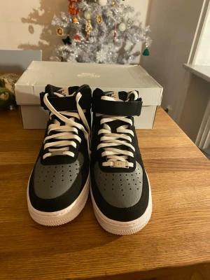 Nike Air Force 1 Mid '07 svart/grå - Säljer ett par Nike Air Force 1 Mid '07 i svart, cool grey och vitt. Skorna har klassisk snörning, kardborreband upptill och perforerad tå. Snygg kontrast mellan svart och grått skinn med vit sula. Perfekta för dig som gillar ikoniska sneakers med streetkänsla.