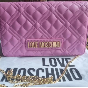 Love Moschino – Klarrosa, quiltad crossbodyväska - Quiltad axelväska från Love Moschino i ljusrosa skinnimitation med guldfärgad kedja. Perfekt storlek för det viktigaste och flera kortfack på insidan. 
