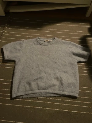 Stickad T-shirt  - Säljer min ljusblåa stickade T-shirt då den inte kommer till användning längre. Den är använd fåtal ggr och ser som ny ut, den är skön och bra passform. 