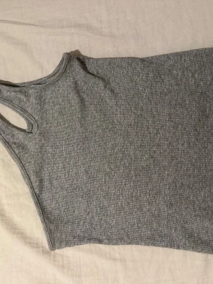 Grå ribbad linnetopp - Säljer en enkel och stilren grå ribbad linnetopp med hög hals och ärmlös design. Perfekt att matcha med jeans eller kjol för en clean look. Materialet är mjukt och stretchigt för extra komfort.