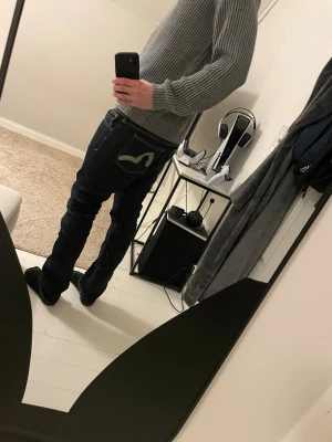 EVISU x Puma jeans W32 L32 - Säljer ett par mörkblå EVISU x Puma jeans med ikoniska gröna målade loggor på bakfickorna. Klassisk rak passform och snygga kontrastsömmar. Tillverkade i bomull med coolt mönstrat innerfoder. Perfekta för dig som vill sticka ut med streetwear-vibe.