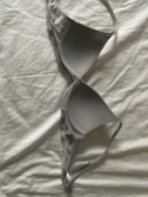 Grå bh med smala axelband - Säljer en enkel och stilren grå bh i mjuk trikå med smala, justerbara axelband. Bh-n har en triangelformad design och är perfekt för lager på lager eller som ett statement-plagg. Passar dig som gillar minimalistisk och avslappnad stil. Storlek 65a.