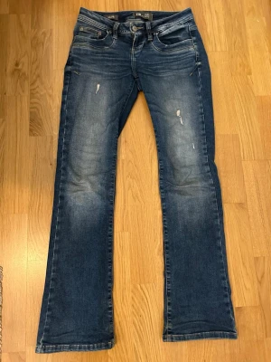 Blå bootcut jeans från LTB Valerie - Säljer ett par blå bootcut jeans från LTB, modell Valerie. Jeansen har slitna detaljer och ljusare partier på låren för en cool, använd look. 