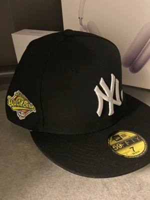 Svart New Era 59FIFTY Yankees keps - Säljer en svart New Era 59FIFTY keps med klassiskt Yankees-broderi framtill och World Series-märke på sidan. Kepsen har broderad text bak och detaljer i vitt. Perfekt för dig som gillar streetwear och sportig stil.