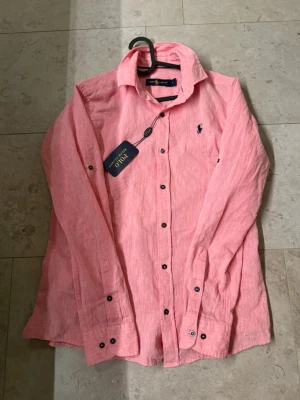 Rosa linneskjorta från Ralph Lauren - Säljer en snygg rosa skjorta från Ralph Lauren i luftigt linne. Perfekt för dig som vill ha en stilren och fräsch look.