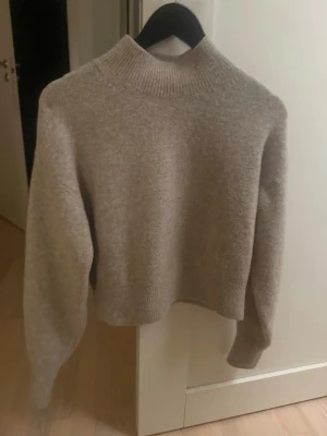 Beige stickad tröja & Other Stories - Mysig beige stickad tröja från & Other Stories med hög ribbad krage och långa ärmar. Tröjan har en loose passform och är perfekt för lager på lager under höst och vinter. Enkel och stilren design som funkar till allt.