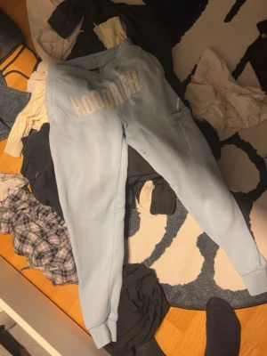 Ljusblå mjukisbyxor från Hoodrich - Säljer ett par ljusblå mjukisbyxor från Hoodrich med stor logga framtill. Byxorna har resår i midjan och muddar vid bensluten samt en ficka på sidan. Perfekta för chill eller streetwear-stil.