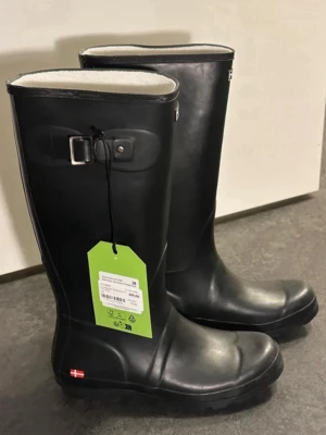 Svarta höga gummistövlar från MOLS - Säljer ett par klassiska svarta gummistövlar från MOLS. De har högt skaft, rund tå och en enkel design med logga upptill. Insidan är fodrad i ljust material och stövlarna har en liten spänndetalj på sidan. Perfekta för regniga dagar.