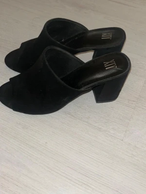 Svarta klackade sandaler från XIT - Säljer ett par svarta sandaler från XIT med öppen tå och bred klack. Skorna har en stilren design i mocka-look och passar perfekt till både jeans och klänning. Supersnygga till sommaren och enkla att matcha med olika outfits.