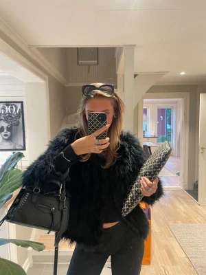 Svart pälsjacka i fuskpäls - Säljer en svart pälsjacka i fuskpäls med croppad passform och långa ärmar. Jackan har en fluffig och lyxig look som verkligen sticker ut. Perfekt för dig som vill ha en statement-piece i garderoben. Fodrad insida för extra komfort. Faux fur jacket