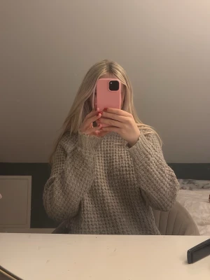 Beige stickad tröja med grov struktur - Mysig beige stickad tröja med grov struktur och avslappnad passform. Tröjan har långa ärmar och ribbade muddar vid ärmslut och nederkant. Perfekt för kyliga dagar och enkel att styla med jeans eller kjol.