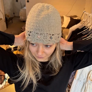 Beige virkad mössa  - Sååå fin beige virkad mössa med blommiga detaljer längs kanten. Mössan är stickad i ett mjukt garn