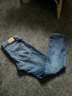 Blå jeans från Nudie Jeans - Säljer ett par klassiska blå jeans från Nudie Jeans med raka ben och snygga kontrastsömmar. Jeansen är modell solid olie. Hör av dig vid frågor!