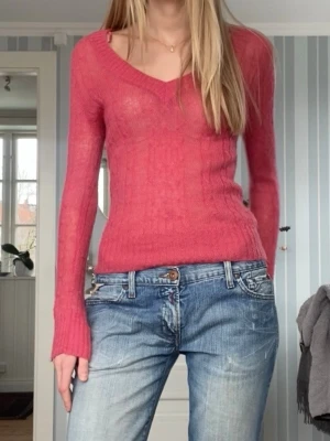 Rosa stickad tröja med v-ringning - Säljer en tunnstickad rosa tröja med v-ringad hals och långa ärmar. Tröjan har en figurnära passform. 25%Mohair, superbra skick