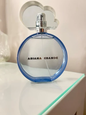 Ariana Grande parfym med molndesign - Snygg parfym från Ariana Grande med unik molnformad kork. Perfekt för dig som vill ha en trendig accessoar på sminkbordet. Flaskan har en modern look som sticker ut och passar dig som gillar popkultur och stilrena detaljer.