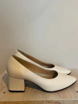 Vita pumps med blockklack och spetsig tå - Stilrena vita pumps med spetsig tå och bred blockklack. Skorna är tillverkade i skinn och har en klassisk, minimalistisk design som passar till många olika looks. Perfekta för dig som gillar en enkel men trendig stil.