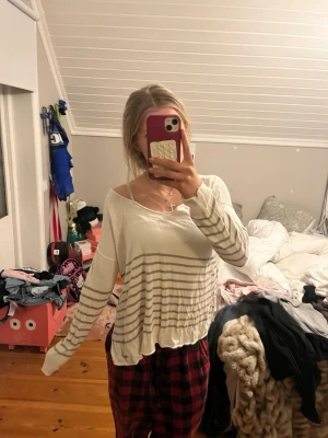 Vit långärmad tröja med ränder - Vit långärmad tröja med beigea horisontella ränder nertill och på ärmarna. Tröjan har en lös och avslappnad passform med bred halsringning. Perfekt för en chill och bekväm stil.