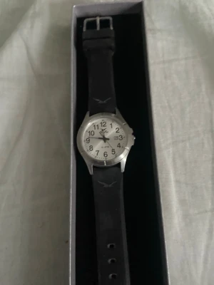 Silverfärgad analog klocka från Q&Q - Stilren klocka från Q&Q med silverfärgat boett och vit urtavla. Svarta siffror och visare gör den lättläst, och den har även datumvisning. Svart armband i gummi ger en sportig känsla. Vattentät till 10 ATM, perfekt för vardagsbruk.