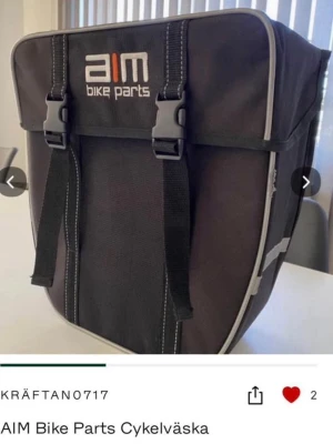 Svart cykelväska AIM Bike Parts (värderad till 800kr) - Praktisk svart cykelväska från AIM Bike Parts med två spännen framtill och reflexdetaljer på sidorna. Väskan har en fyrkantig form och är tillverkad i slitstark polyester, perfekt för att fästa på cykeln och ta med dina grejer.