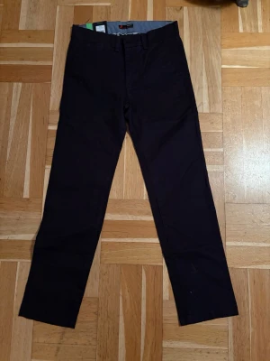 Svarta chinos från Wrangler - Snygga svarta chinos. Byxorna har bälteshällor, knapp och dragkedja framtill samt två bakfickor med knapp. Även fickor fram. Nya med prislapp kvar