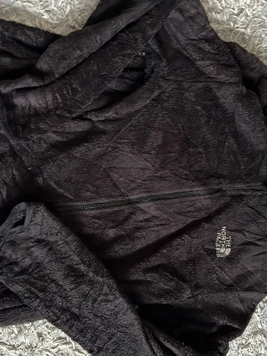 Svart fleecejacka från The North Face - Mjuk och fluffig svart fleecejacka från The North Face med dragkedja framtill och broderad logga på bröstet. Perfekt för lager-på-lager och håller dig varm under kyliga dagar. Klassisk passform och hög krage.