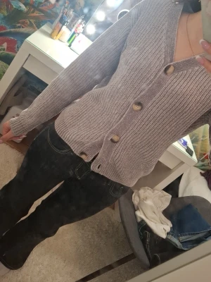 Ljuslila ribbad kofta med knappar - Mysig ljuslila kofta med stora knappar och ribbad struktur. Koftan har v-ringning och lång ärm, perfekt för lager på lager. Passar till både jeans och kjol för en chill look. Aldrig använda därför säljes