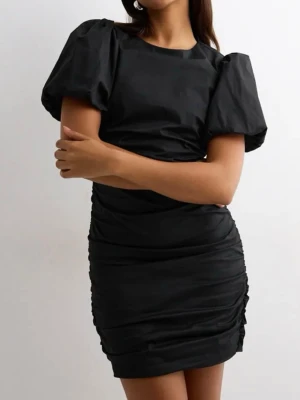 Svart puffärm kortklänning - Säljer en svart kortklänning med puffiga korta ärmar och rynkade detaljer längs sidorna och ryggen. Klänningen har en figurnära passform och rund halsringning. 