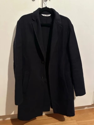 Mörkblå rock från Zara - Stilren mörkblå rock från Zara med klassisk krage och två knappar framtill. Kappan har raka linjer, två fickor och är helfodrad. 