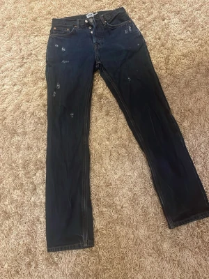 Levi's 501 mörkblå jeans med slitningar - Mörkblå Levi's 501 jeans med klassisk rak passform och snygga slitningar framtill. Jeansen har knäppning med knappar, fem fickor och är tillverkade i robust denim. Perfekta för en avslappnad och trendig look.