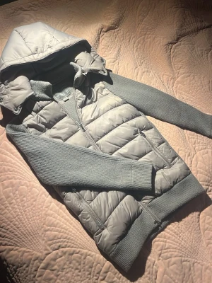 Grå cardigan jacka med huva - Snygg grå cardigan jacka från Leon Marcél med quiltad kropp och stickade ärmar. Jackan har dragkedja framtill, två fickor med dragkedja och avtagbar huva. Perfekt för lager på lager och chill stil.