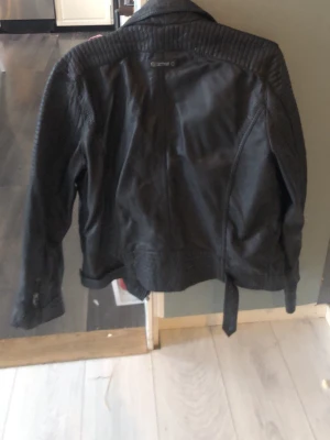 Svart skinnjacka från Gipsy - Snygg svart skinnjacka från Gipsy med klassisk bikerstil. Jackan har långa ärmar, markerade axlar och bälte i midjan. Perfekt för dig som vill ha en cool och tidlös look.