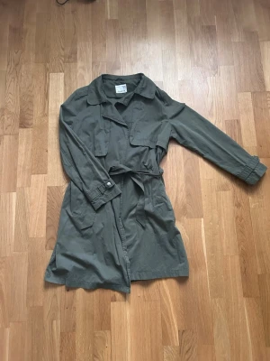 Olivgrön trenchcoat med bälte - Stilren olivgrön trenchcoat från Zara med klassisk krage, knytskärp i midjan och långa ärmar med knappdetalj vid mudden. 💕