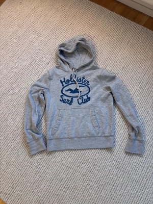 Holister Surf Club hoodie - Säljer denna galet snygga Holister hoodien med ett snyggt och stilrent tryck framtil. Skön hoodie som går att matcha till mycket.   |   Kommer från djur och rökfritt hem | Storlek M men sitter som S/M