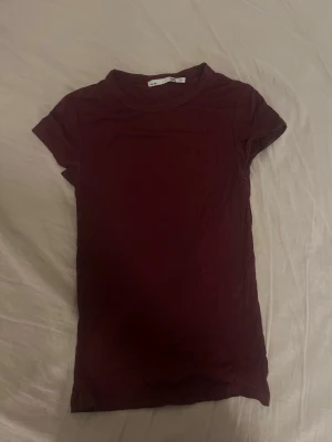 Vinröd t-shirt från 157 - En enkel och stilren vinröd t-shirt från lager 157 i storlek XS. T-shirten har rund halsringning och korta ärmar. Tillverkad i mjuk bomull som känns skön mot huden. Perfekt basplagg att matcha med jeans eller kjol.