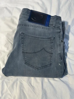 Grå jeans från Jacob Cohën 622 - Snygga grå jeans från Jacob Cohën med klassisk femficksdesign och diskret logopatch bak. Jeansen har rak passform och är tillverkade i mjukt bomullsmaterial med en hint av stretch för extra komfort. Modell 622 (slim fit). 