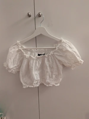 Vit off shoulder blus från Bik Bok - Supersöt vit off shoulder blus från Bik Bok i storlek XS. Blusen har broderade hål, volangkant upptill och nertill samt puffiga korta ärmar Kort i modellen. Perfekt för sommarens alla tillfällen och ger en romantisk vibe.                                                               Pris kan diskuteras vid smidigt köp 😊                        Köparen står för frakt!