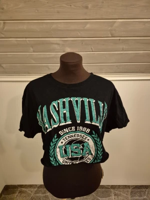 Nashville t-shirt - Croppad svart t-shirt med stort tryck i grönt och vitt där det står 'Nashville USA Tennessee'🦎🇱🇷 Köpt i USA och bara använd några få gånger. Det är bara att skriva om man har frågor!😊💖