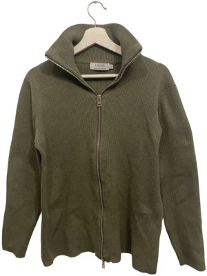 Olivgrön ziptröja från Ljung - Säljer en olivgrön ribbstickad ziptröja från Ljung by Marcus Larsson. Tröjan har hög krage, dragkedja framtill och är tillverkad i ett mjukt stickat material. Perfekt för lager på lager och enkel att styla till olika outfits.