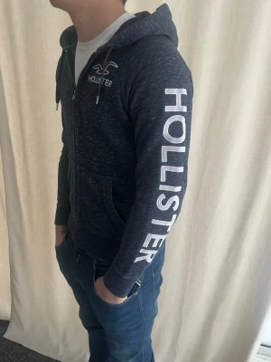 Hollister hoodie - Sjukt snygg hoodie från hollister i storlek S. Trycket på armen är riktigt schysst. Personen på bilderna är 184 cm. Skicka prisförslag. Kika in min profil för liknande plagg