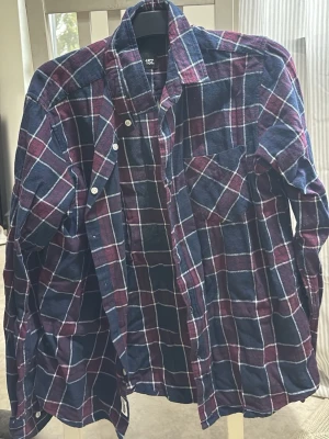 Rutig skjorta från Lager 157 i blått och vinrött - Klassisk rutig skjorta från Lager 157 i mörkblått, vinrött och vitt. Skjortan har lång ärm, bröstficka och knappar framtill. 