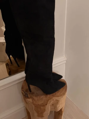 Svarta höga mockastövlar med klack - Snygga svarta stövlar i mocka med spetsig tå och hög klack. Stövlarna går upp över knät och har en elegant, smal siluett som passar perfekt till både kjol och jeans. Klassisk och trendig modell 