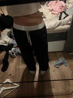 Svarta mjukisbyxor med vit midja - Svarta mjukisbyxor med bred vit resår i midjan och vit snörning framtill(på insidan som man kan vika ned om man vill). Byxorna har en loose passform och raka ben, vilket ger en chill och avslappnad vibe. Perfekta för att hänga hemma,dansa eller dra till gymmet. Materialet känns mjukt och bekvämt mot huden.