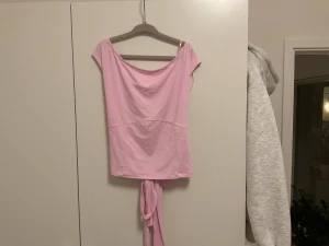 Ljusrosa omlottopp med knyt - Säljer en rosa topp. Toppen har en öppen rygg och är tillverkad i mjuk bomull. Snygg! Gina 14+ xs