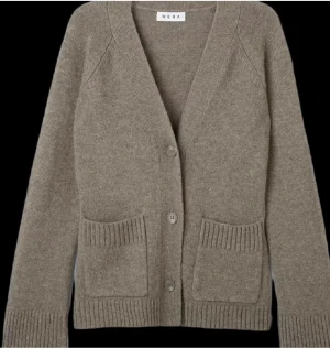 Beige kofta från Wera med fickor - Mysig beige kofta från Wera med v-ringad hals och ribbade detaljer. Koftan har två praktiska fickor framtill och stängs med tre knappar. Perfekt för lager-på-lager och chill dagar. Passar dig som gillar enkel och stilren look.