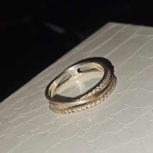 Silverring med glittriga stenar - Snygg silverring med två rader små glittriga stenar runt hela ringen. Ringen har en elegant och modern design med detaljerade kanter som ger extra bling. Perfekt för dig som gillar stilrena smycken med lite extra sparkle.